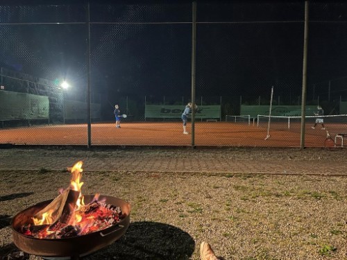 Tennisspiel bei Nacht mit Feuerschale im Vordergrund